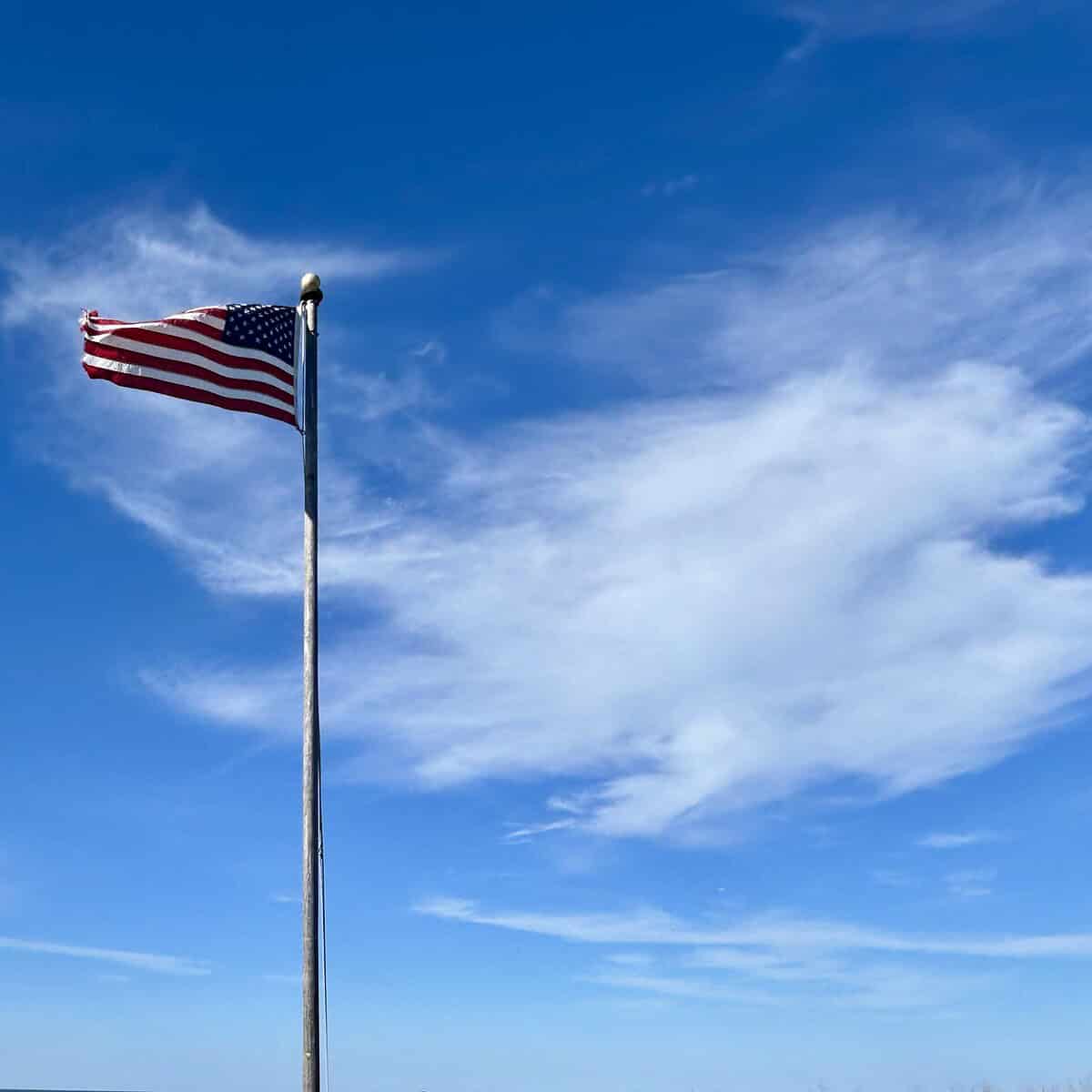 American flag on flagpole with beachgrass, clouds, and sea in the background